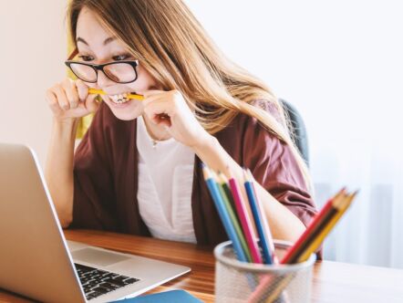 Persoon achter diens laptop, met potlood in diens mond. Kijkt nieuwsgierig naar het scherm.