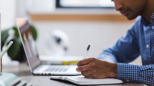 Man zit achter zijn computer met een pen in zijn handen.
